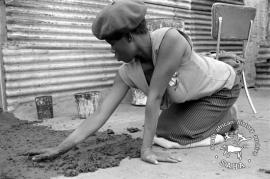 This black and white photograph of a woman making a mud and dung floor at her house in Braklaagte was taken by Gille de Vlieg on 9 October 1986. Included in SAHA Land Act Project report, 2014.