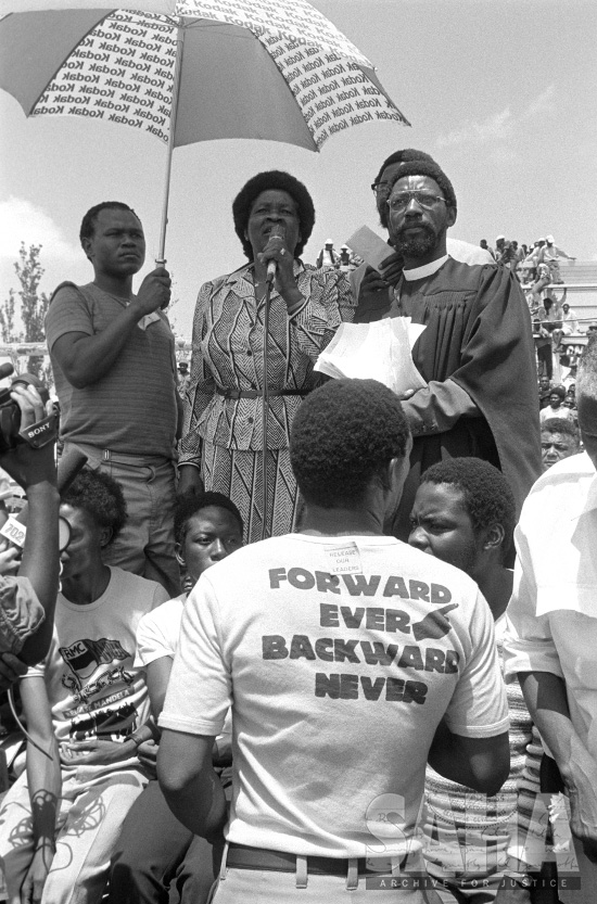 AL3274_D08.8The Gille de Vlieg Photographic Collection. D8.8 Albertina Sisulu speaks, Nyami Booi holds the umbrella, Alexandra, Gauteng, 1986-03-05