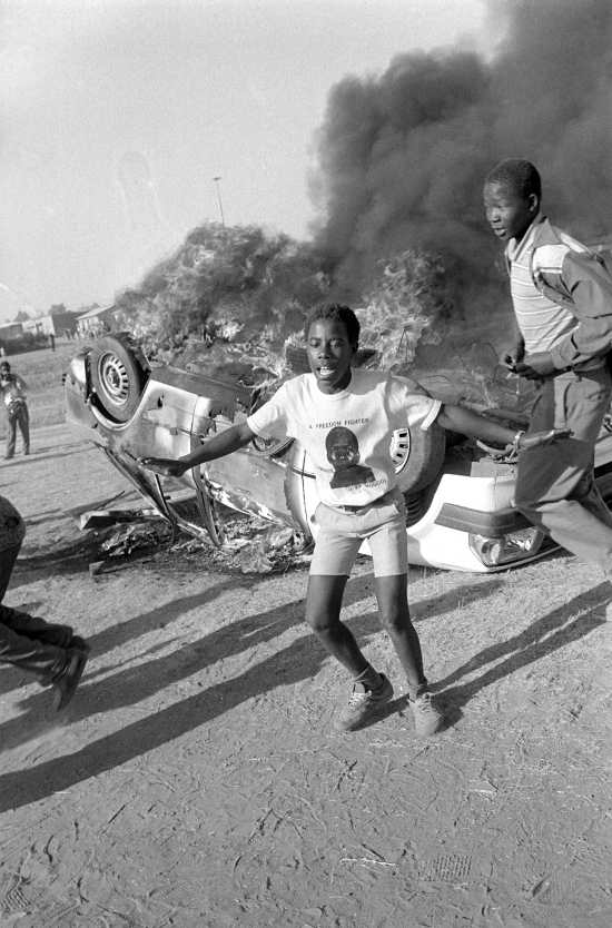 Suspected informer's car burns (Bishop Tutu rescued the informer) and youth celebrate, Duduza, Gauteng, 1985-07-10. Photograph by Gille de Vlieg